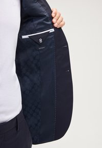 Blazer blu navy con una vestibilità extra slim, caratterizzato da una fodera testurizzata, tasca interna e dettagli di cucitura a contrasto lungo il bordo.