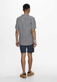 Korte mouwen overhemd met marineblauwe en witte verticale strepen, gebogen zoom en achterpand. Gecombineerd met marineblauwe shorts en tan schoenen.