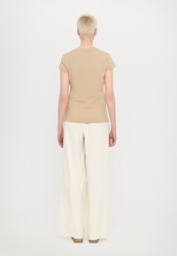 Beige přiléhavé tričko s krátkým rukávem, spárované s širokými bílými kalhotami. Oblečení má jednoduchý design a jemnou texturu, viděné ze zadu.