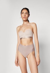 Beige stropløs bh med en glat tekstur og et bånd med en subtil glans, kombineret med højtaljede, lysebeige trusser.