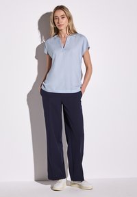 Blusa azzurro chiaro a maniche corte con scollo a V, abbinata a pantaloni navy larghi e sneakers bianche. Tessuto morbido, design rilassato.