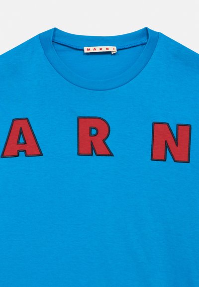 Zils kokvilnas T-krekls ar īsām piedurknēm, uz priekšpuses ar lielām sarkanām izšūtām burtiem "A", "R" un "N". Apaļš kakla izgriezums.