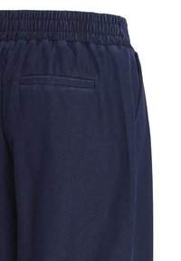 Pantalon bleu marine avec taille élastique et poche arrière fendue sur fond blanc