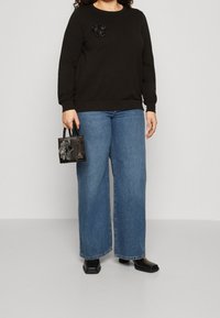 Black sweatshirt with a floral accent, paired with wide-leg blue denim jeans. A small black handbag with decorative accents in hand.