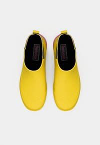 Chaussures en caoutchouc jaune à enfiler, avec une texture lisse, un bout arrondi, des accents roses au talon et une semelle intérieure de marque.