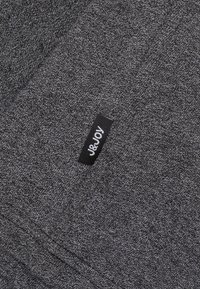 Grijs fleeceachtige stof met een gestructureerd patroon, voorzien van een genaaide zwarte label met witte tekst "J&JOY" aan de rand.