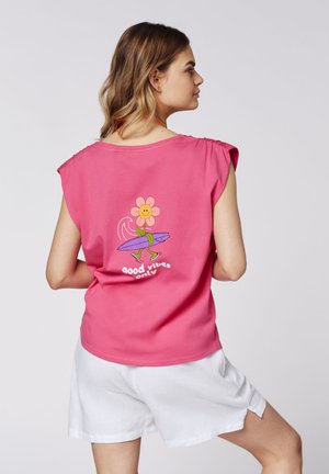 Pink cotton sleeveless t-shirt featuring a graphic of a flower with a smiley face holding a surfboard, displaying the text "good vibes only."