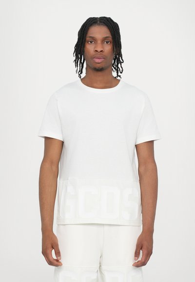T-shirt en coton blanc à col rond, avec des manches courtes et un logo "GCDS" blanc contrastant en bas. Texture douce et coupe décontractée.