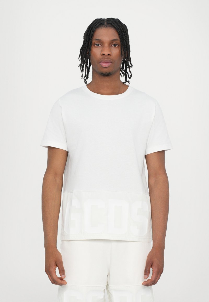 Maglietta in cotone bianco con scollatura rotonda, maniche corte e logo "GCDS" bianco a contrasto nella parte inferiore. Tessuto liscio e vestibilità rilassata.