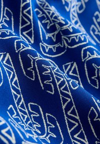 Kék szövet fehér geometriai és cikkcakk mintákkal, közeli részletekben, textúrával és redőkkel.