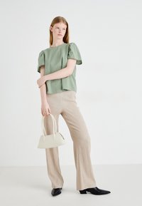 Svijetlozeleni majica kratkih rukava s teksturiranim tkaninom, uparena s bež hlačama visokog struka sa uzorkom i bijelom torbicom. Cipele s oštrim vrhom crne boje.