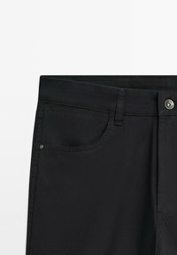 Zwarte denim broeken met een voorzak, een metalen knoopsluiting en een naadloze tailleband met minimale stiksels en geen zichtbare patronen.