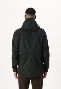 Black hooded jacket with elastic waist, textured fabric, and side pockets, featuring a relaxed fit and long sleeves.