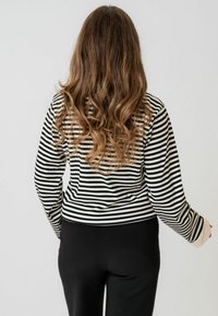 Dugi rukav crno-bijeli prugasti top s rebrastom teksturom, s čvrstim rukavima u krem boji i prilagođenim dizajnom. Nosene su crne hlače.