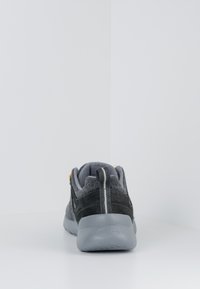 Graue und schwarze Sneaker mit einem weichen Textil-Obermaterial, Gummisohle, gestreiftem Detail auf der Rückseite und einer Fersenlasche. Subtile Strukturvariation.