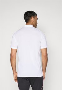Hvid kort�ærmet polo skjorte med krave, der har en glat tekstur og minimalistisk design. Bæres sammen med sorte shorts med lyserøde striber.