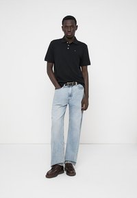 Schwarzes Polohemd, hellblaue weit geschnittene Jeans und braune Schuhe. Das Outfit weist ein klassisches Design mit einer schlichten Silhouette und Denim-Textur auf.