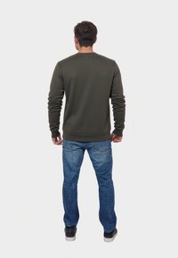 Felpa verde con colletto rotondo e maniche lunghe, abbinata a jeans blu. Presenta polsini e vita a coste, con un'etichetta logo sul retro.