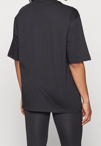 Black oversized t-shirt made of smooth fabric, featuring short sleeves, a rounded neckline, and a straight hem. No visible logos or patterns.