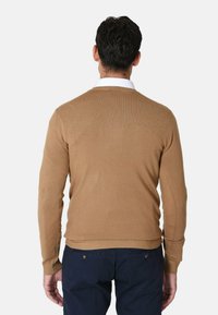 Maglione a maglia color beige con collo rotondo e polsini a coste, visto da dietro, abbinato a pantaloni blu scuro. Texture liscia, design aderente.