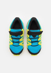 Blue and yellow athletic shoes with textured fabric, adjustable strap, and black accents. Features a cushioned interior and lace design.