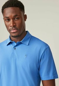 Helles blaues Poloshirt aus weichem Stoff, mit Kragen, Knopfleiste und einem kleinen gestickten Logo auf der linken Brust.