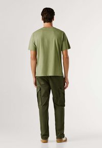Camiseta de manga corta en verde oliva, hecha de algodón, combinada con pantalones cargo a juego que presentan bolsillos laterales y un ajuste relajado.