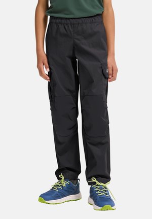 Person trägt schwarze Cargo-Hosen mit elastischen Bündchen und blaue Turnschuhe mit limettengrünen Schnürsenkeln und steht vor einem weißen Hintergrund.