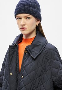 Ναυτικό μπουφάν με καπιτονέ ραφές, φαρδύ γιακά, χρυσά κουμπιά πατιλέτα και φερμουάρ. Συνδυασμένο με πλεκτό σκούφο σε ναυτικό μπλε και πορτοκαλί πουλόβερ με ριμπ ύφανση.