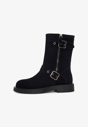 Schwarzer Wildleder-Stiefelette mit rundem Zehenbereich, seitlichem Reißverschluss und zwei verstellbaren Riemen mit metallischen Schnallen und Nieten am Schaft.