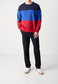 Sudadera con bloques de color en azul marino, azul y rojo, hecha de tela suave, con cuello redondo, combinada con pantalones negros y zapatillas blancas.