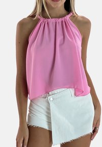 Różowy top bez rękawów z marszczonym dekoltem, wykonany z lekkiego materiału, w połączeniu z białymi szortami o skośnym kroju z postrzępionymi brzegami.