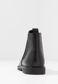 Botín Chelsea de cuero negro con paneles elásticos en los laterales, puntera redonda y un tacón bajo apilado. Textura suave con detalles de costura visibles.