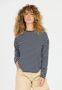 Navy en wit gestreepte langekatoenen shirt met een ontspannen pasvorm en ronde halslijn, gecombineerd met beige shorts.