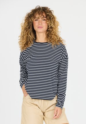 Navy en wit gestreepte langekatoenen shirt met een ontspannen pasvorm en ronde halslijn, gecombineerd met beige shorts.