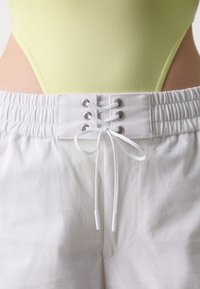 Witte shorts met een gladde textuur, voorzien van een elastische tailleband en een frontale vetersluiting met zilveren oogjes.