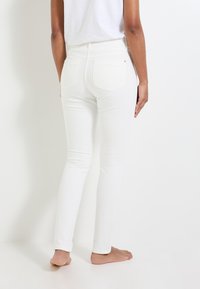 Jeans blancos ajustados con una textura suave, de tiro alto y dos bolsillos traseros. La tela parece elástica y se ajusta al cuerpo.
