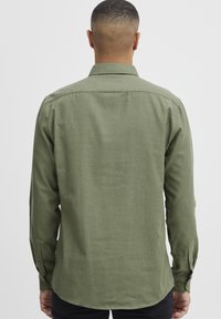 Green, long-sleeve shirt made of textured fabric with a button-down collar and cuffs, featuring a straight cut and a back yoke.