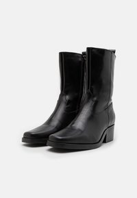 Botas de cuero negras hasta el tobillo con un diseño elegante, punta redondeada y un tacón cuadrado moderado. Cuentan con una cremallera lateral para facilitar su uso.