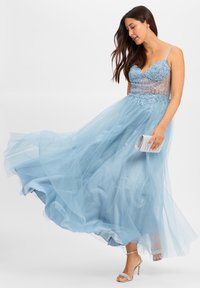 Abito da sera azzurro chiaro con corpino di perline, gonna in tulle e accenti scintillanti. Abbattutto con tacchi argentati a cinghietta e una pochette coordinata.
