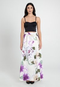 Top corto nero con spalline sottili. Gonna lunga e fluida con un motivo floreale in viola, verde e beige su uno sfondo bianco.