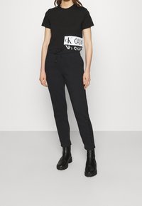 Svart kortärmad t-shirt med vit logodetalj, matchad med svarta joggers med sidotryck, bärs med svarta ankelstövlar. Enkel, strömlinjeformad design.