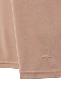 Tissu beige avec des coutures visibles et un petit logo d'arbre en relief près du bord inférieur.