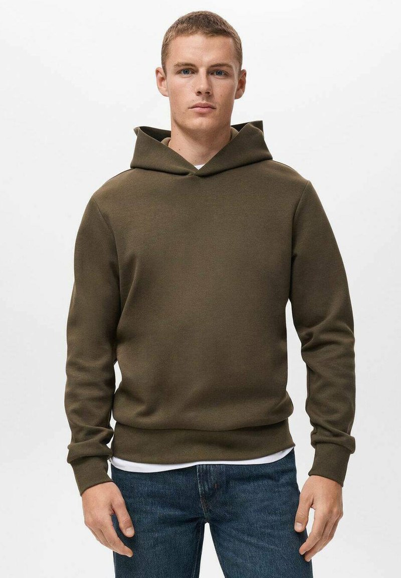 Olijfgroene hoodie gemaakt van zachte, textuurstof; heeft een grote capuchon, geribbelde manchetten en een rechte zoom. Draagt over een wit shirt.