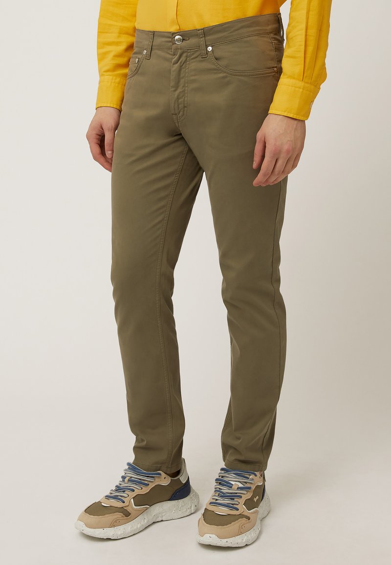 Chinos verdes de corte slim, con bolsillos frontales, una textura suave y costuras resistentes. Combinados con zapatillas de tonos neutros.