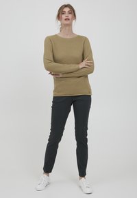Kaki värvi kudum, millel on tekstuuriline disain, ümar kaelus ja pikad varrukad, kombineeritud kitsaste mustade pükste ja valgete tossudega.