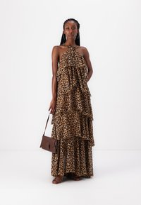 Haljina maxi s uzorkom leoparda, s halter dekolteom i slojevitim volanima. U paru s smeškanom smeškom i sandalama s trakama.