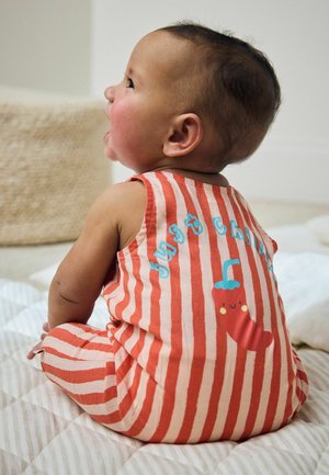 Baby sidder på en quiltet overflade iført en rød og hvidt striped outfit med en sød chili grafik og "just chili" tekst på ryggen.