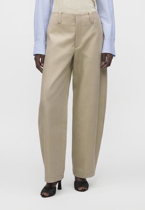 Béžové široké nohavice s vysokým pásom v kombinácii so svetlomodrou košeľou s dlhým rukávom, zastrčenou dovnútra, a čiernymi otvorenými topánkami na podpätku.
