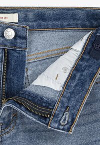 Blugi din denim cu o spălare albastru închis. Include un nasture argintiu, fermoar și cusături contrastante portocalii. Căptușeala este dintr-un material textil alb.